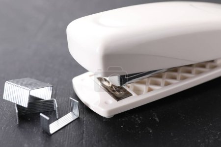 Beige stapler with staples on black textured table, closeup
