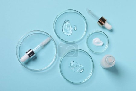 Photo for Petri dishes with samples of cosmetic serums, bottle and pipettes on light blue background, flat lay - Royalty Free Image