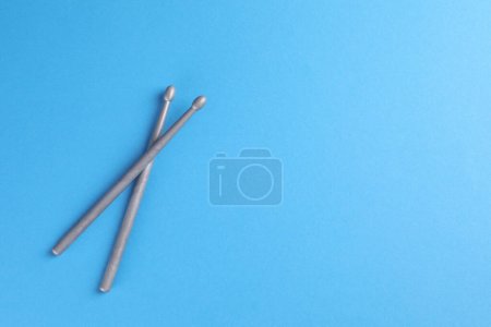 Two gray drum sticks on light blue background, top view. Space for text