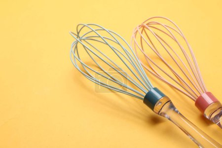Two whisks on yellow background, closeup. Space for text