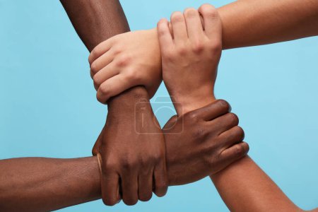 Photo for Men joining hands together on light blue background, closeup - Royalty Free Image