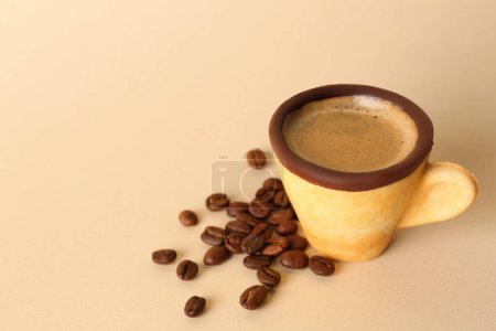 Foto de Deliciosa taza de galletas comestibles con café expreso y granos de café sobre fondo beige. Espacio para texto - Imagen libre de derechos