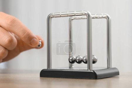 Man playing with Newton's cradle at table against light background, closeup. Physics law of energy conservation