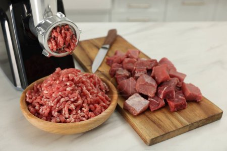 Electric meat grinder with beef on white marble table indoors