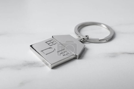 Metal keychain in shape of house on marble table, closeup