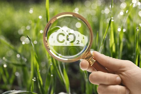 Reduce CO2 emissions. Woman demonstrating CO2 inscription through magnifying glass outdoors, closeup