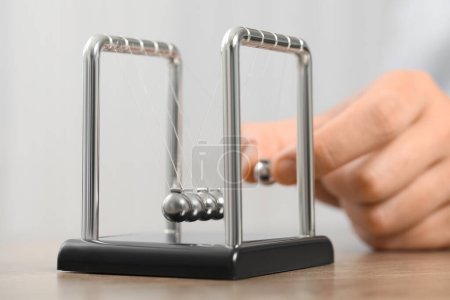 Man playing with Newton's cradle at table against light background, closeup. Physics law of energy conservation