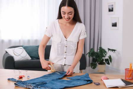 Happy woman making ripped jeans at table indoors
