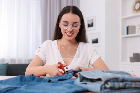 Happy woman cutting hem of jeans at table indoors