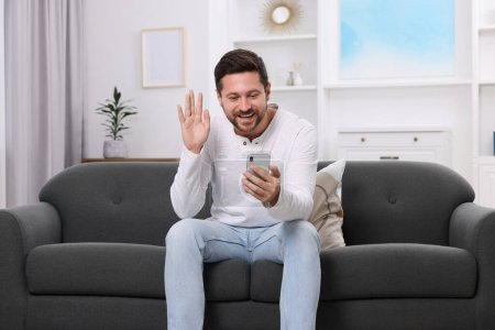 Happy man greeting someone during video chat via smartphone at home
