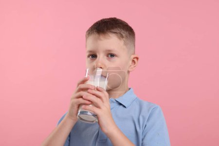 Téléchargez les photos : Mignon garçon boire du lait frais à partir de verre sur fond rose - en image libre de droit