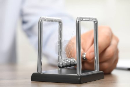 Man playing with Newton's cradle at table, closeup. Physics law of energy conservation