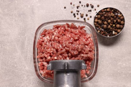 Manual meat grinder with beef mince and peppercorns on light grey table, flat lay