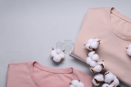 Cotton branch with fluffy flowers and t-shirts on light gray background, flat lay. Space for text