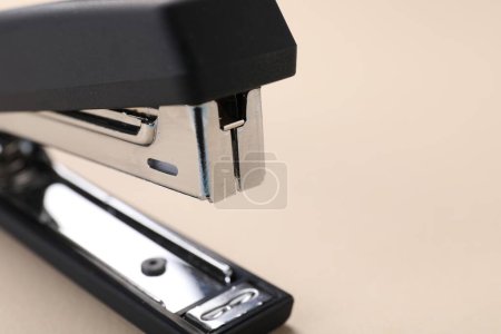 Black stapler s on beige background, closeup. Space for text
