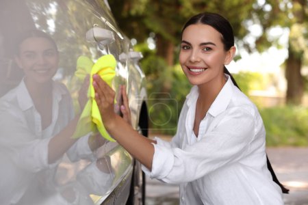 Téléchargez les photos : Femme heureuse nettoyage porte de voiture avec chiffon à l'extérieur - en image libre de droit