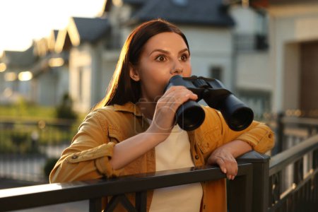 Concepto de vida privada. Mujer joven y curiosa con prismáticos espiando a los vecinos sobre la valla al aire libre