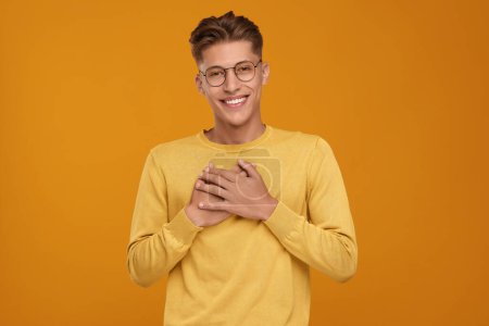 Thank you gesture. Happy grateful man with hands on chest against orange background