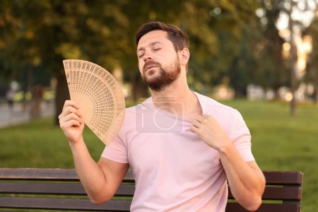 Hombre con ventilador de mano que sufre de calor al aire libre