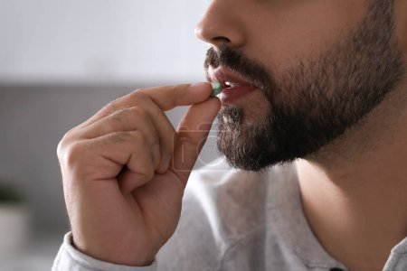 Man taking antidepressant pill on blurred background, closeup