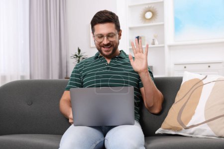Happy man greeting someone during video chat via laptop at home