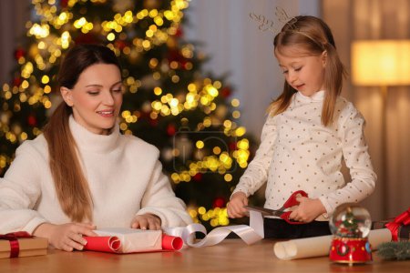 Geschenkpapier zu Weihnachten. Mutter und ihre kleine Tochter dekorieren Geschenkbox mit Schleife zu Hause
