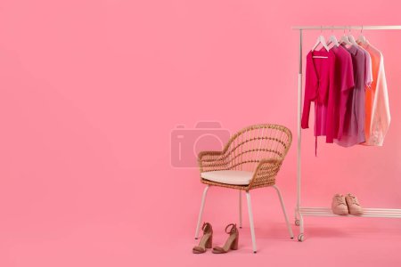 Support avec différents vêtements, chaussures et fauteuils élégants pour femmes sur fond rose, espace pour le texte