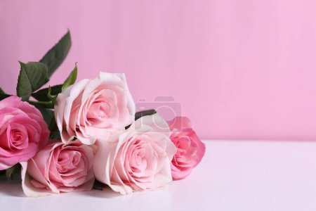 Photo for Beautiful roses on light table against pink background, closeup. Space for text - Royalty Free Image