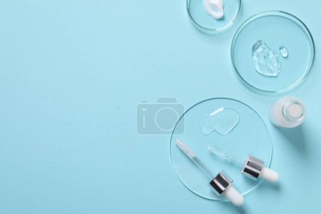 Photo for Petri dishes with samples of cosmetic serums, bottle and pipettes on light blue background, flat lay. Space for text - Royalty Free Image