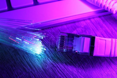 Optical fiber strands transmitting different color lights near cable with modular connector and computer keyboard on table, closeup