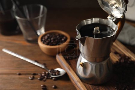 Brewed coffee in moka pot and beans on wooden table, closeup