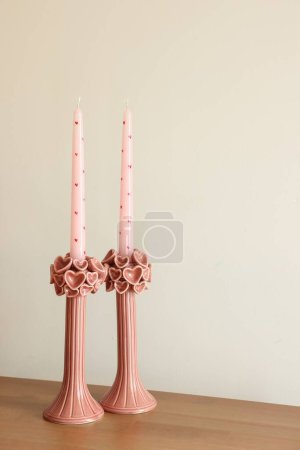 Téléchargez les photos : Belles bougies en cire rose sur table en bois près du mur blanc - en image libre de droit
