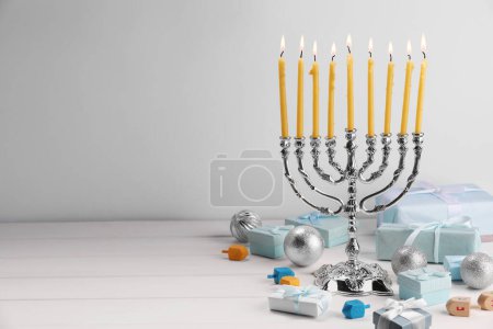 Téléchargez les photos : Hanoukka fête. Menorah avec des bougies allumées, des dreidels, des boîtes-cadeaux et des ornements de vacances sur une table en bois blanc, espace pour le texte - en image libre de droit