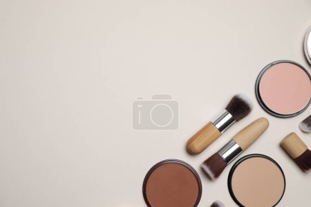 Téléchargez les photos : Différentes poudres pour le visage et pinceaux de maquillage sur fond beige, plat. Espace pour le texte - en image libre de droit