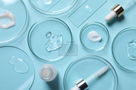 Platos Petri con muestras de sueros cosméticos, botella y pipetas sobre fondo azul claro, puesta plana