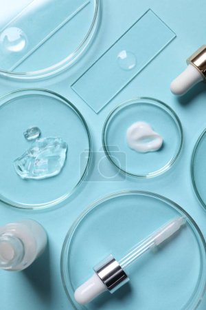 Photo for Petri dishes with samples of cosmetic serums, bottle and pipette on light blue background, flat lay - Royalty Free Image