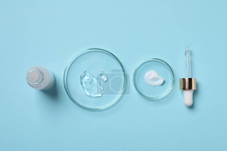 Photo for Petri dishes with samples of cosmetic serums, bottle and pipette on light blue background, flat lay - Royalty Free Image