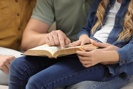 Chica y sus padrinos leyendo la Biblia juntos en el interior, primer plano