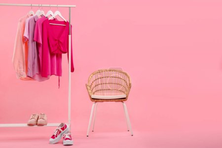 Support avec différents vêtements élégants pour femmes, baskets et fauteuils sur fond rose, espace pour le texte