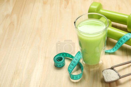 Tasty shake, dumbbells, measuring tape and powder on wooden table, space for text. Weight loss