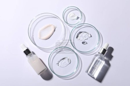Platos Petri con muestras de sueros cosméticos y botellas sobre fondo blanco, planas