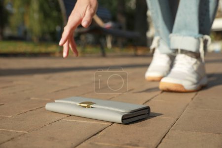 Photo for Woman picking up grey purse outdoors, closeup. Lost and found - Royalty Free Image