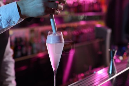 Bartender adding foam onto alcoholic cocktail at counter in bar, closeup. Space for text