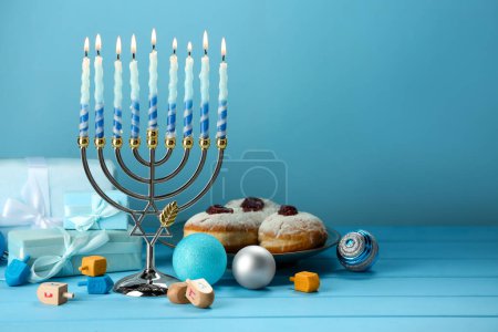 Komposition mit Chanukka Menora, Dreidels, Donuts und Geschenkschachteln auf einem Tisch vor hellblauem Hintergrund. Raum für Text