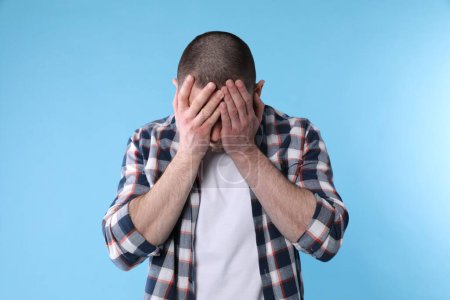 Photo for Upset man closing his face with hands on light blue background - Royalty Free Image
