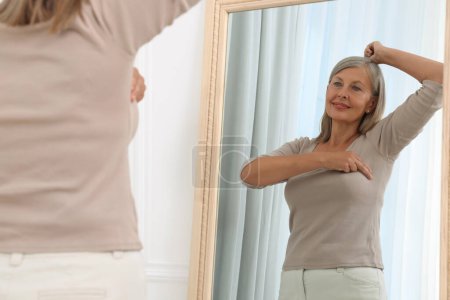 Belle femme âgée faisant l'auto-examen du sein près du miroir à l'intérieur