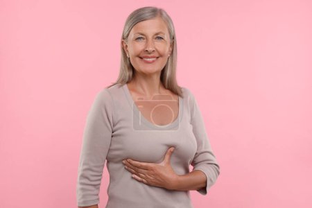 Beautiful senior woman doing breast self-examination on pink background