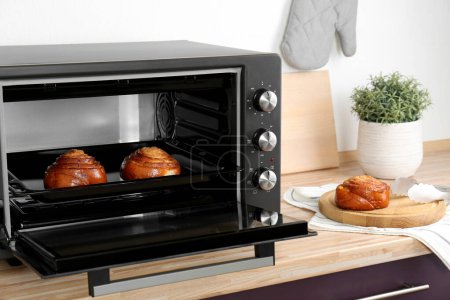 Open electric oven with delicious pastry on wooden table in kitchen