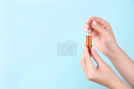 Photo for Woman holding bottle of essential oil on light blue background, closeup. Space for text - Royalty Free Image