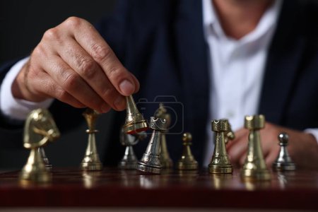 Homme avec pièce de jeu jouant aux échecs au damier sur fond sombre, gros plan
